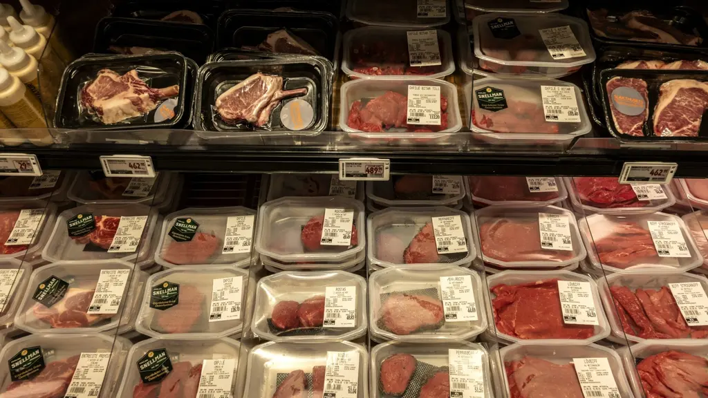 En hylla i en matbutik fylld med förpackat kött, inklusive nötkött och andra köttprodukter. Prislappar och etiketter syns tydligt på förpackningarna.