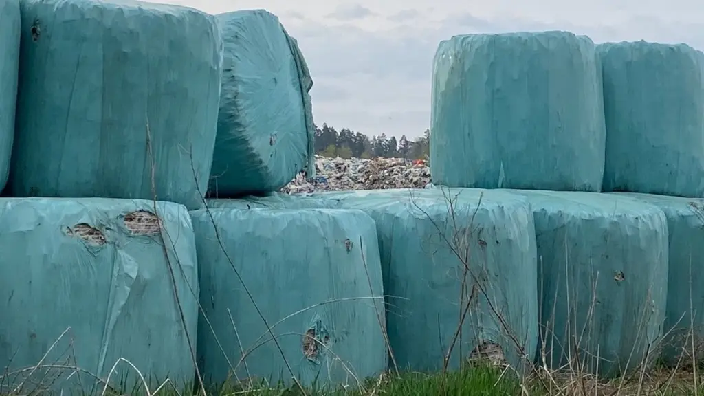 Sopbalar inslagna i blå plast står staplade på Skultunatippen utanför Västerås, omgivna av gräs och med skog i bakgrunden. Himlen är molnig.