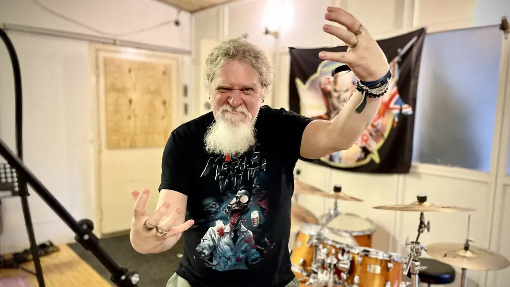 Jörgen Kristensen, säljare på Musikbörsen i Västerås och medlem i banden Dead Awaken och Centinex, står framför ett trumset i en musikstudio och gestikulerar med händerna.
