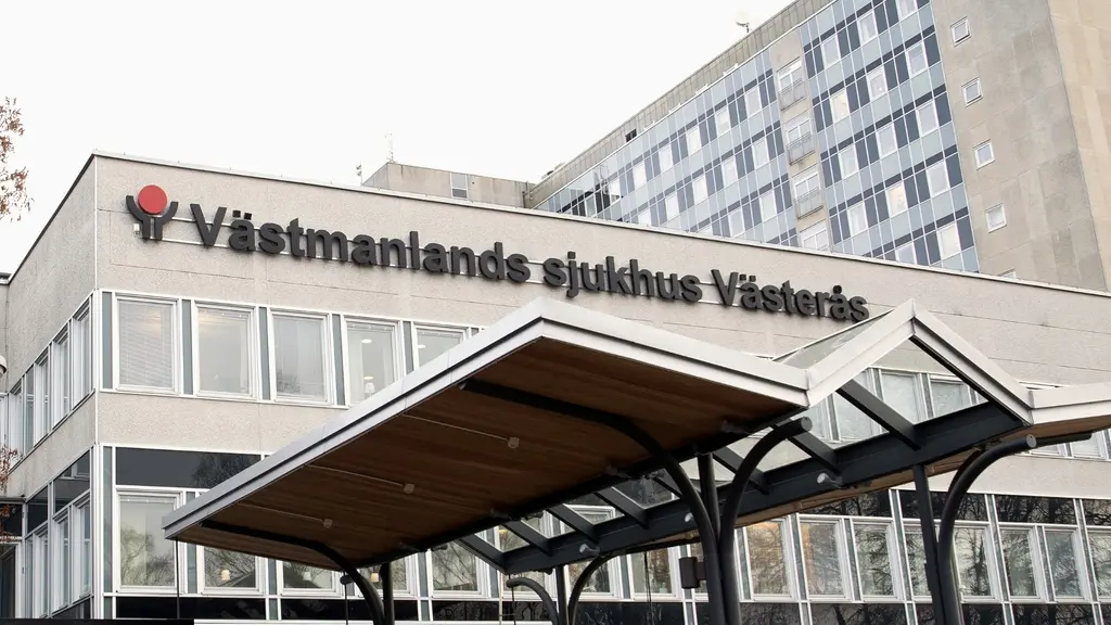 Västmanlands sjukhus i Västerås med en stor byggnad i bakgrunden och ett tak över entrén i förgrunden. Sjukhusets namn syns tydligt på fasaden.