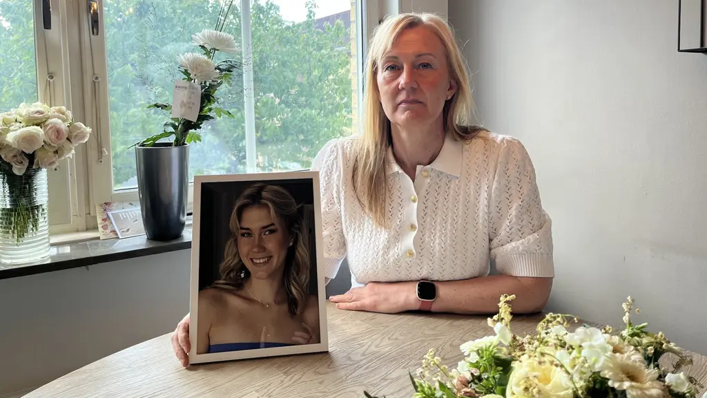En kvinna sittandes i köket. Bredvid henne är ett fotografi på hennes dotter. Hon tittar in i kameran med en serös blick.Alicia, 20, dog i cancer – fick aldrig modern protes