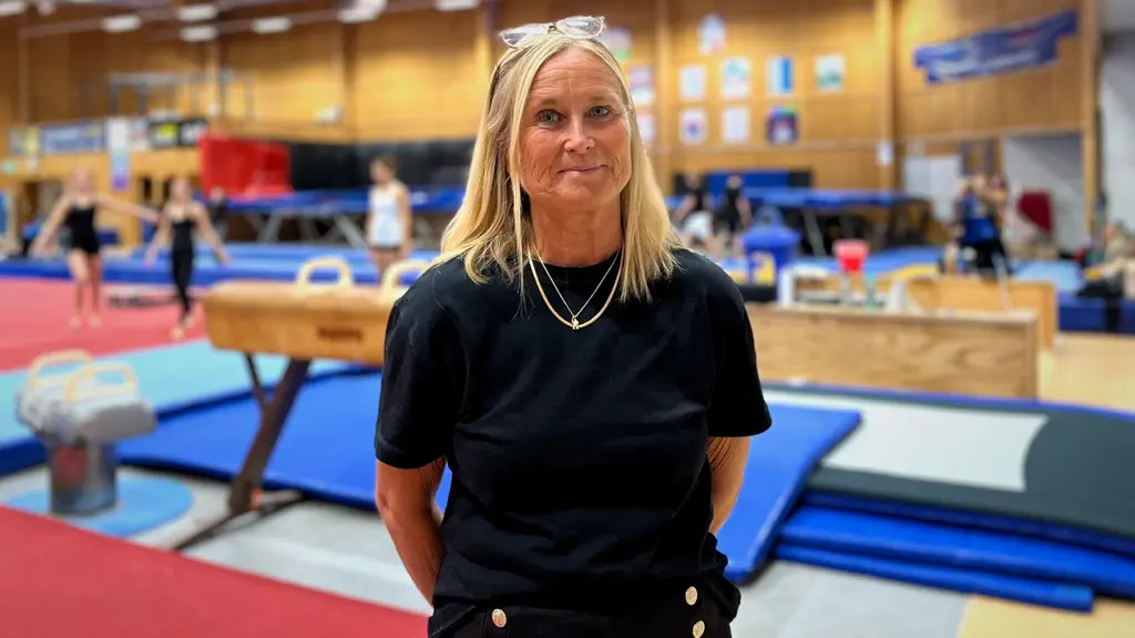 Christine Almskoug, verksamhetschef för gymnastik- och cheerleadingföreningen Uppsala, står i en gymnastikhall med redskap och mattor i bakgrunden.