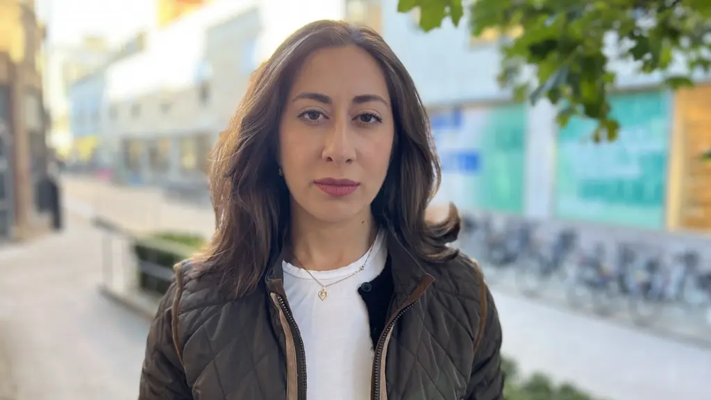 Asal Gohari står utomhus på en stadsgata med grönska och byggnader i bakgrunden. Hon har mörkt hår, en mörk jacka och en vit tröja.