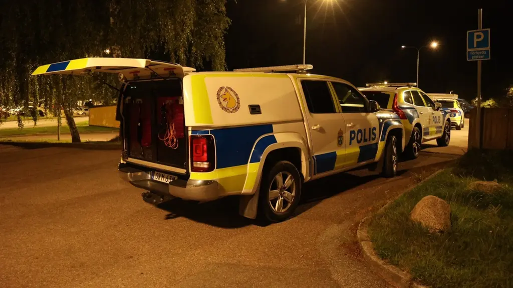 Polisbilar står parkerade i ett bostadsområde. Bakluckan på ett av fordonen är öppen och området är upplyst av gatubelysning.