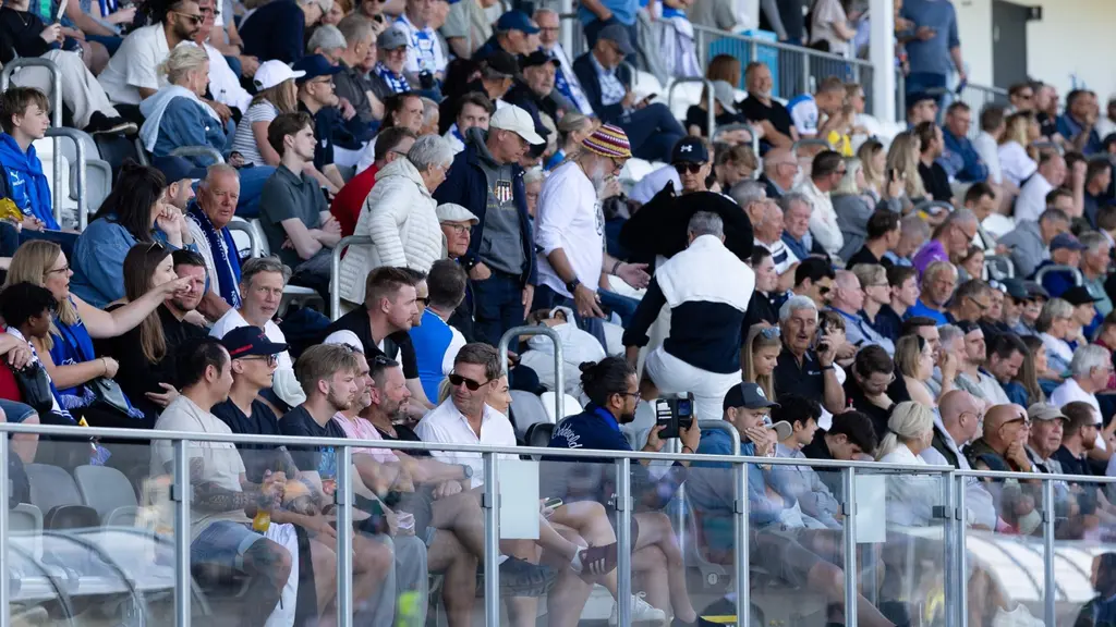 Publikhav på läktaren under mötet mellan Oddevold och Ljungskile, med tätt sittande supportrar i sommarkläder och fullsatta rader bakom glasräcke.