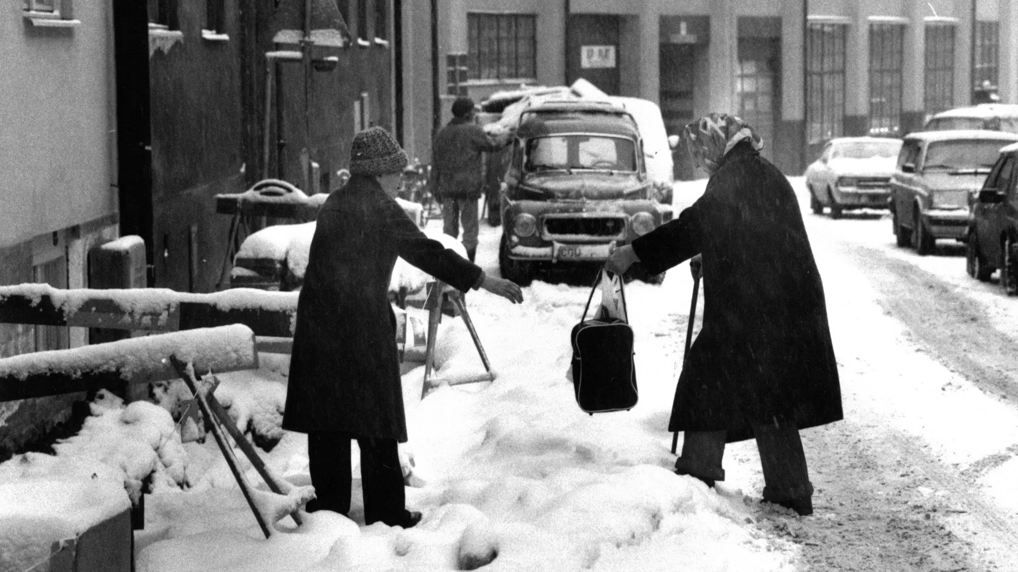 En kvinna räcker ut en hjälpande hand åt en annan kvinna som går på en snöig gata.