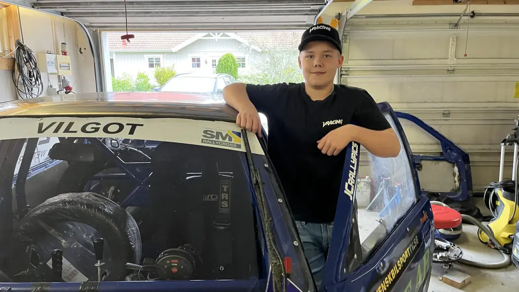 Vilgot Wetter står vid sin rallycrossbil i ett garage, klädd i svart t-shirt och jeans. Bilen har hans namn på vindrutan och är blå med racingdetaljer.