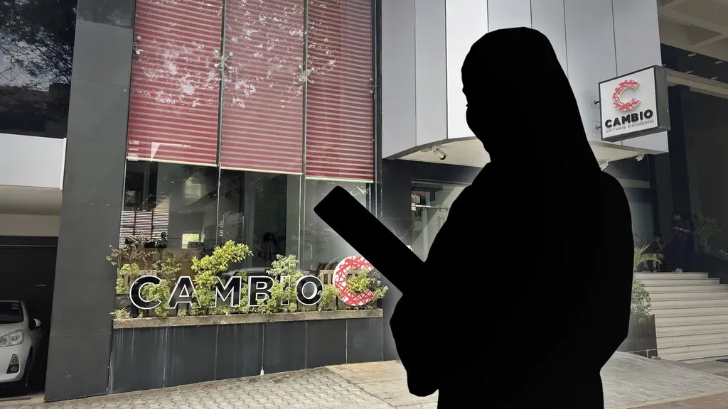 En silhuett av en person som håller i ett dokument framför en modern byggnad med glasfasad och skyltar. Byggnaden är omgiven av växter och har en tydlig ingång.