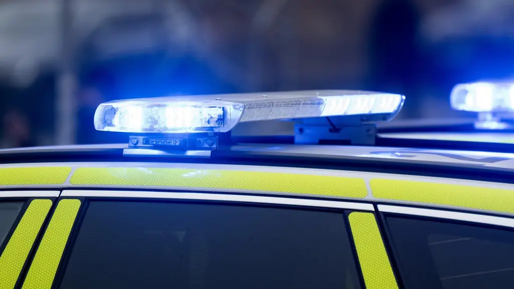 Närbild på en polisbil i Stockholm med aktiverade blåljus. Bilden visar taket och delar av bilens gula och svarta mönster, vilket signalerar pågående polisinsats.