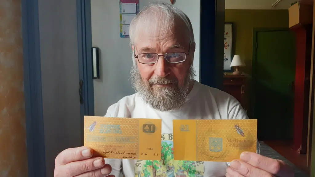 Kjell Holmstrand sitter ned med blicken rakt in i kameran. Han håller upp två sedlar framför sig, Klövern. Han visar sedelns fram och baksida. Valören är 1 klöver