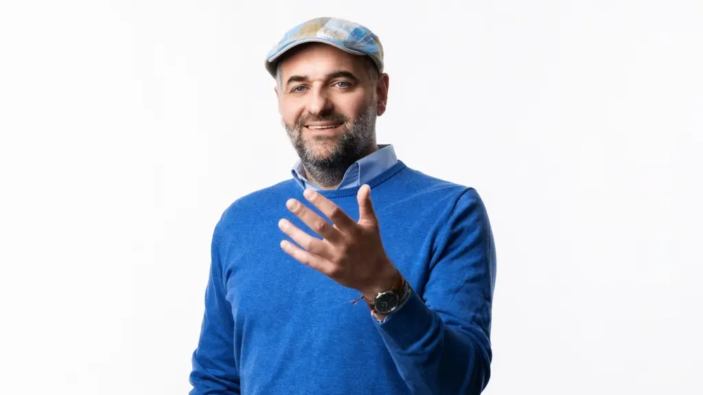 En man i blå tröja och keps som håller fram ena handen.
