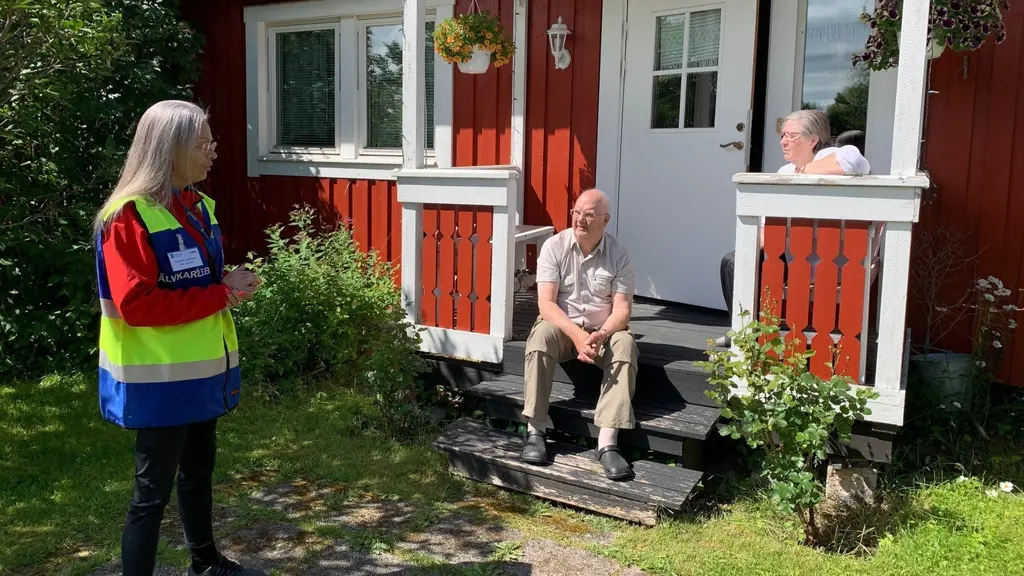 Äldre par sitter på farstutrappan. Volontär på besök.