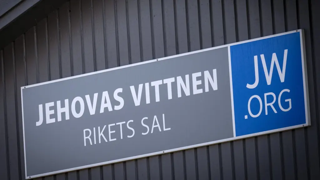 Skylt på fasad med texten 'Jehovas Vittnen Rikets Sal' och logotypen 'JW.org', fotograferad i centrala Älmhult.