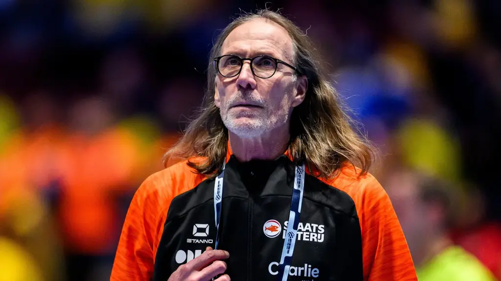 Person med suddat ansikte i svart och orange funktionärskläder står på arenaområdet med ackreditering runt halsen, mot suddig publikbakgrund.