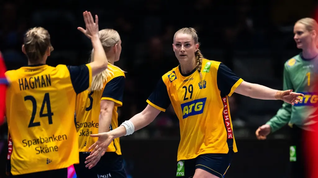 Tre handbollsspelare i gula matchtröjor firar på planen under en handbollsmatch. Nummer 24, Hagman, syns tydligt med ryggen mot kameran. Spelarna ser ut att vara mitt i ett firande.