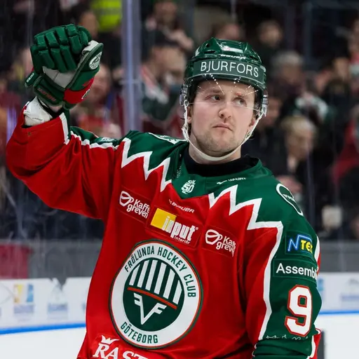 En ishockeyspelare i Frölunda HC:s röda matchtröja jublar med höjd knytnäve på isen. I bakgrunden syns åskådare på läktaren.