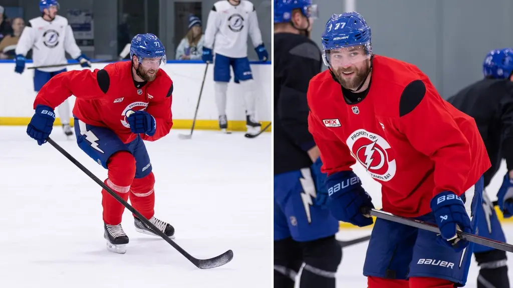 En hockeyspelare, identifierad som Victor Hedman, är klädd i en röd träningströja som signalerar att han inte får tacklas. Han håller en hockeyklubba och befinner sig på en ishockeyrink under träning.