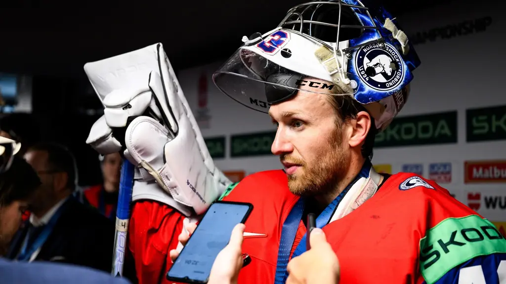 Norges målvakt Henrik Haukeland i hockeyutrustning intervjuas i mixed zone efter VM-bronsmatchen i ishockey, med hjälm och plockhandske nära ansiktet.
