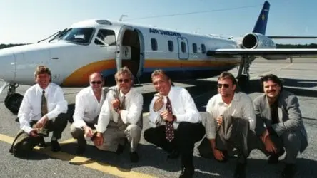 Dansbandet Vikingarna framför sitt eget flygplan på Bromma flygfält. De sitter på huk på plattformen framför flygplanet. Christer Sjögren sitter i mitten. Foto: : Janerik Henriksson/SCANPIX 1995