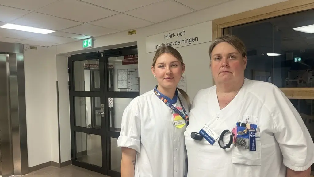 Two women in nurses uniforms in a hospital corridor.