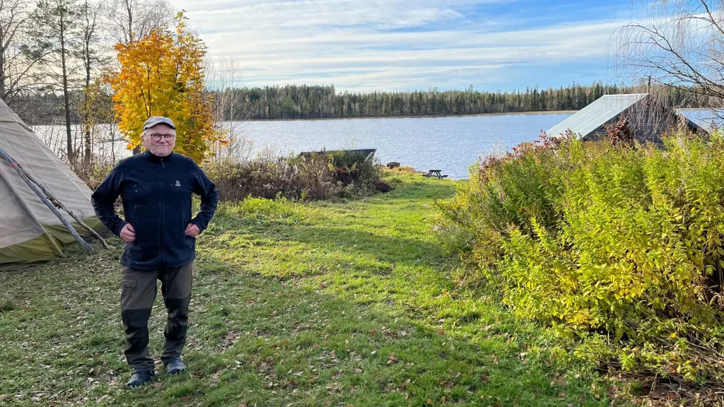 En man står vid en tältkåta vid en sjö en solig höstdag i Tornedalen. 