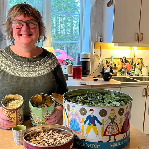 Kvinna med glasögon står med diverse torkad kvanne i färg glada plåtburkar 