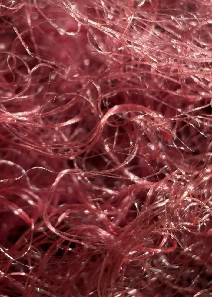 Närbild av rosa och glänsande spindeltråd skapad med hjälp av bakterier. Trådarna är tunna och sammanflätade, vilket ger en textur av mjuka och komplexa mönster.
