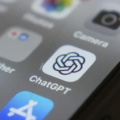 En närbild på en smartphone där appen ChatGPTs ikon syns tydligt på skärmen. Ikonen är placerad bland andra appar som kamera- och väderappar. Skärmen är mörk och detaljerna är skarpa.