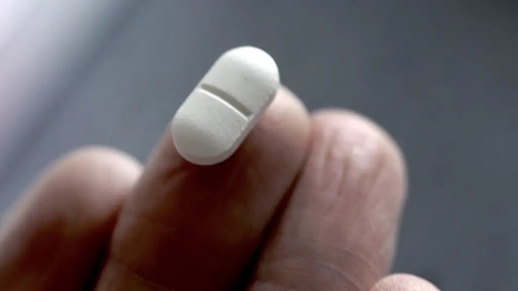 En vit medicintablett hålls mellan fingertopparna mot en mörk bakgrund. Tabletten diskuteras som möjlig behandling för att hindra återfall av cancer.