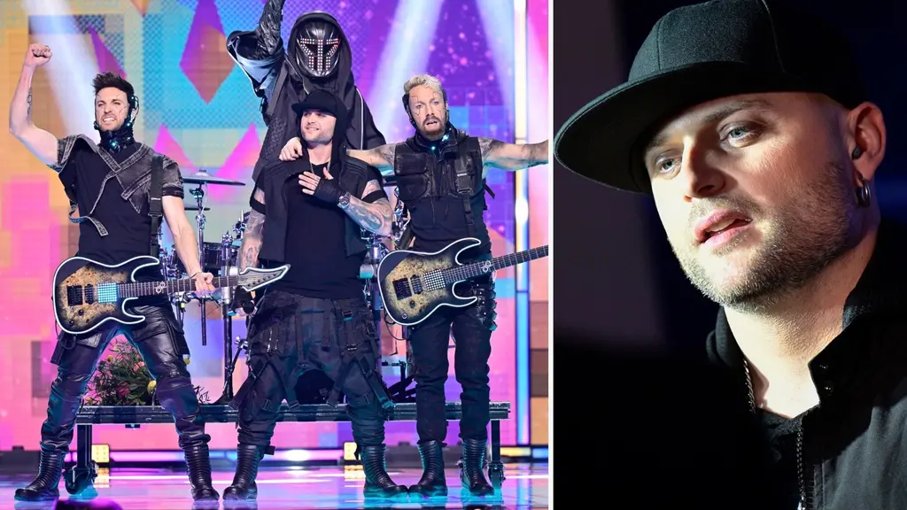 En musikgrupp framför på en färgglad scen, klädda i svarta scenkostymer och med elgitarrer. Bakom dem syns trummor och en dekorativ bakgrund.