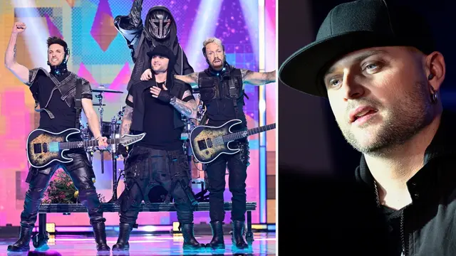 En musikgrupp framför på en färgglad scen, klädda i svarta scenkostymer och med elgitarrer. Bakom dem syns trummor och en dekorativ bakgrund.