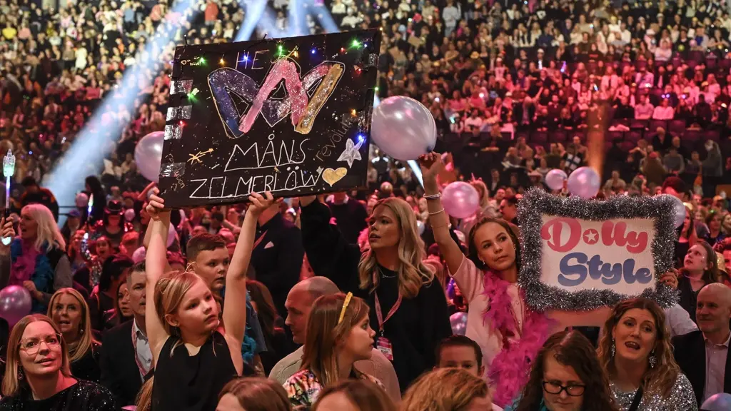 Publiken på Melodifestivalens final 2025 i Strawberry Arena, Stockholm. Fans håller skyltar med text som hyllar Måns Zelmerlöw och Dolly Style under en färgsprakande kväll.