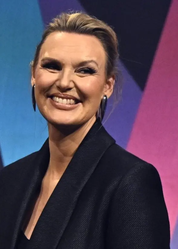 En person i mörk kavaj står framför en färgglad bakgrund med geometriska former under en presskonferens för Melodifestivalen 2026 i Stockholm.