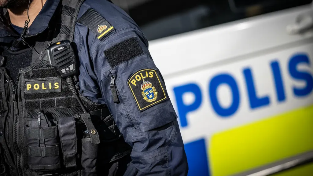 En svensk polis i uniform står framför en polisbil med tydliga polismarkeringar. Fokus ligger på polisens emblem och uniformens detaljer. Bilden symboliserar polisiär närvaro i Malmö vid larm om misstänkt föremål.
