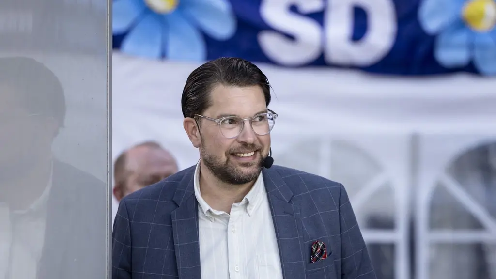 Jimmie Åkesson framför en stor SD-band­eroll med blommor i bakgrunden.