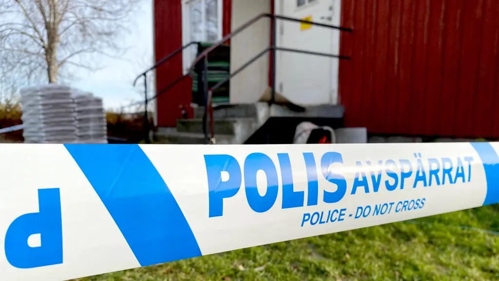 Polisavspärrning framför ett hus med röd fasad.