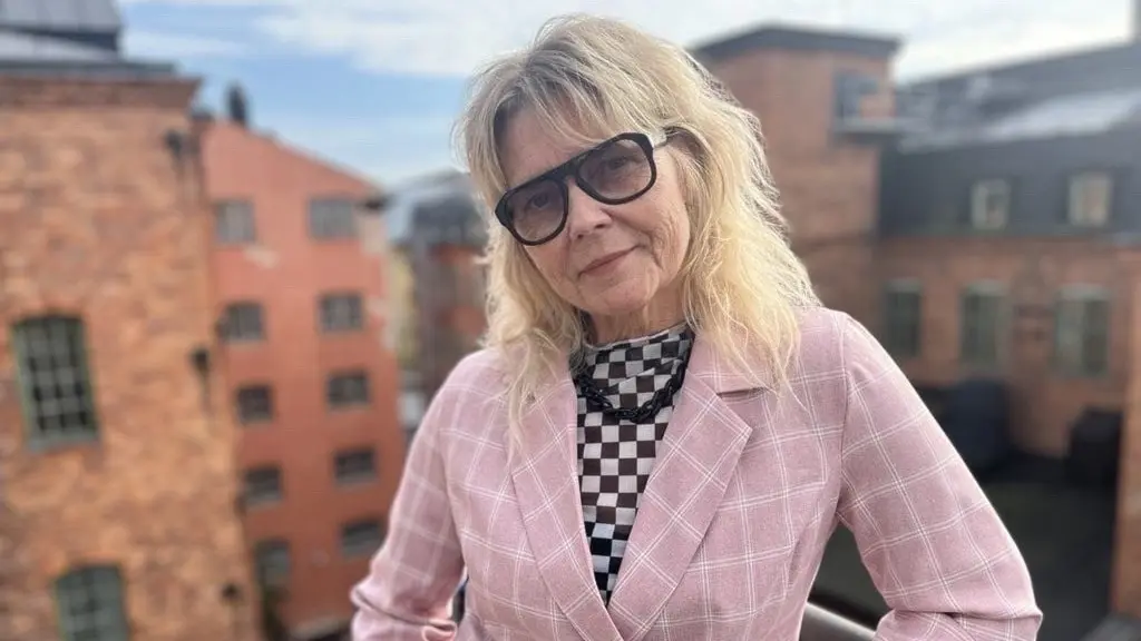 Kvinna som står i Norrköpings industrilandskap. Bär rosa kavaj och glasögon. 