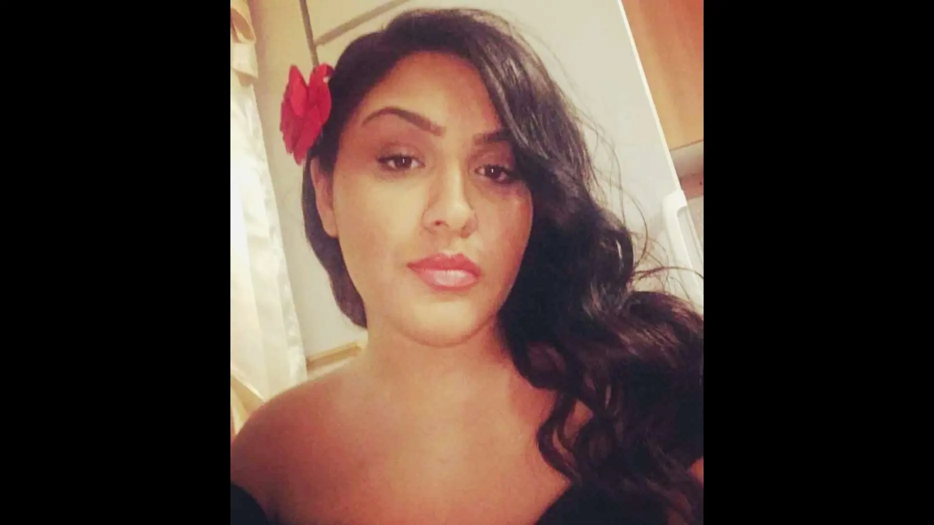 Kvinna med blomma i håret tittar in i kameran. 