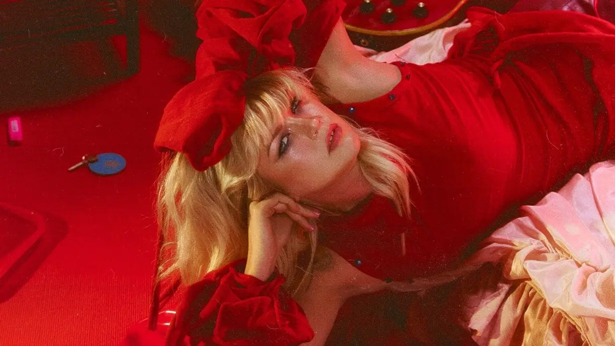 Bild på artisten Maria Jane Smith klädd i rött liggandes på en säng.