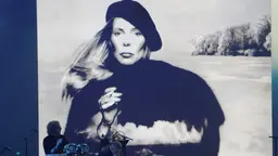 Sångerskan och låtskrivaren Joni Mitchell hyllas i Las Vegas 2022. Bakom musikerna på scenen syns hon på omslaget till sitt album "Hejira" från 1976.