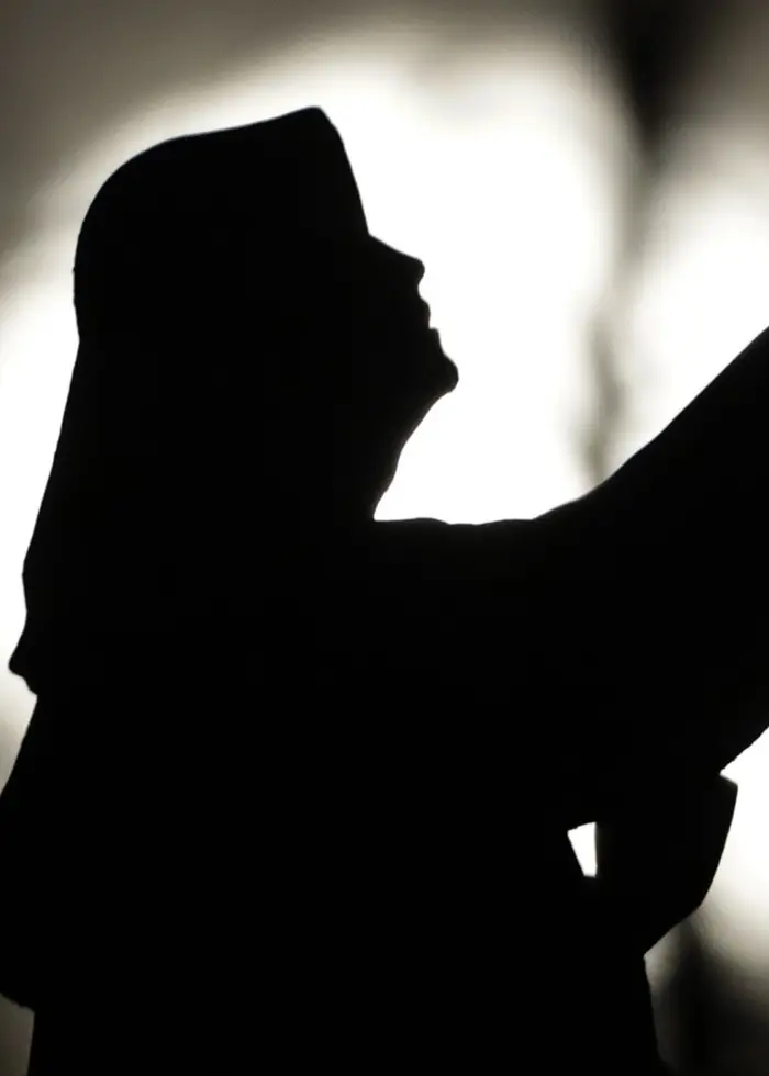 En silhuett av en religiös staty syns mot en ljus fullmåne i bakgrunden. Statyn föreställer en figur i en lyft gest, placerad i en mörk och dramatisk miljö.