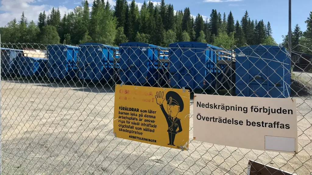 Blå containrar på rad och i förgrunden ett stängsel med skyltar på.