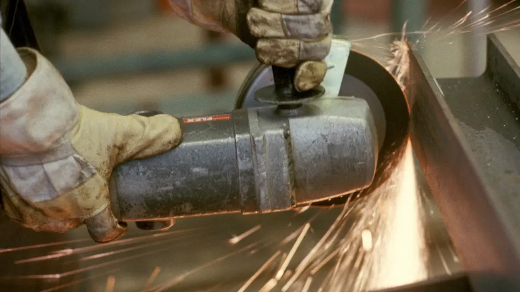 En arbetare använder en vinkelslip på en metallverkstad, gnistor flyger medan verktyget skär genom metallen. Bilden visar detaljerade handskar och verktyg i en industriell miljö.