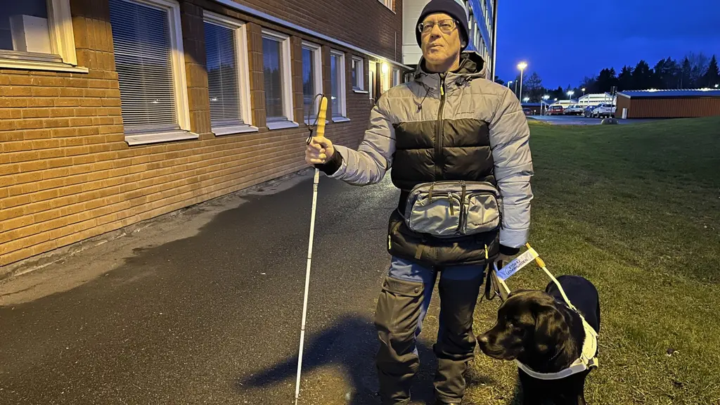 En man i vinterkläder med vitkäpp och ledarhund.