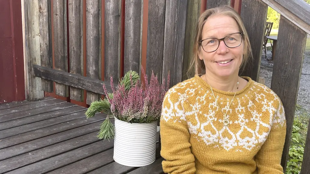 Anna-Karin Roos, överläkare på neurologimottagningen vid Östersunds sjukhus, sitter utomhus vid ett träbord med en blomkruka innehållande ljung och gröna växter.
