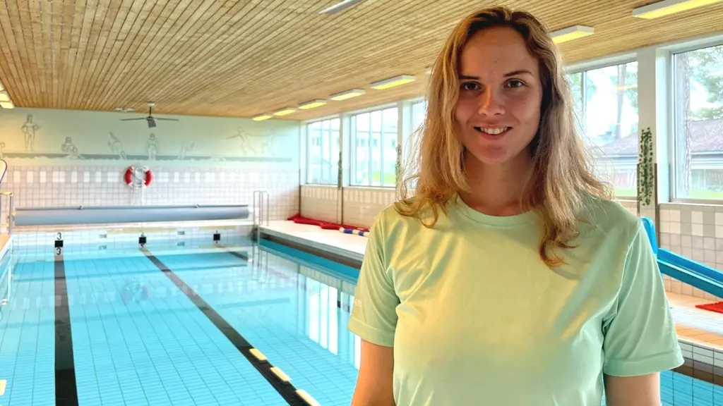 Jelena Nääs står vid inomhuspoolen i Svenstavik. Simlärare och engagerad i Svenska Livräddningssällskapet framför en simhall med lugnt vatten och stora fönster.