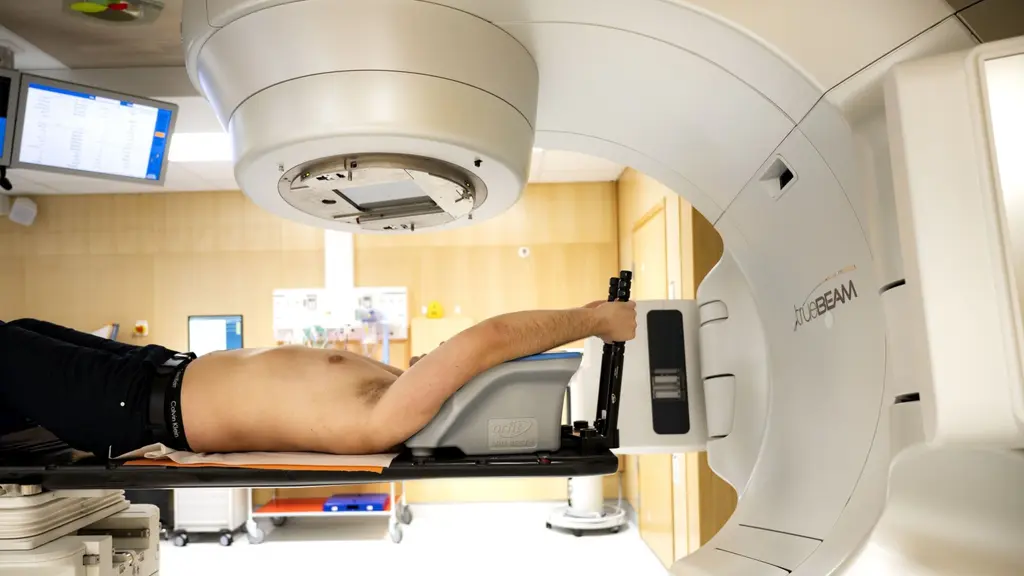 En patient ligger på en brits under en stor strålningsmaskin för behandling av en tumör på en canceravdelning på Karolinska universitetssjukhuset i Solna. Genrebild.