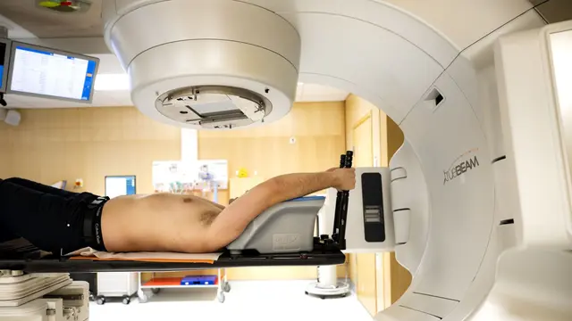 En patient ligger på en brits under en stor strålningsmaskin för behandling av en tumör på en canceravdelning på Karolinska universitetssjukhuset i Solna. Genrebild.