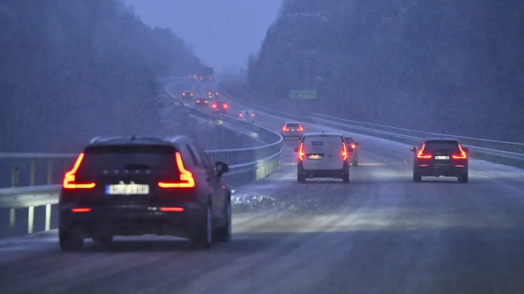 Snöfall på E18 mellan Bålsta och Enköping med flera bilar som kör på den vintertäcka vägen. Sikten är begränsad och vägbanan är hal, vilket påverkar trafiksituationen.