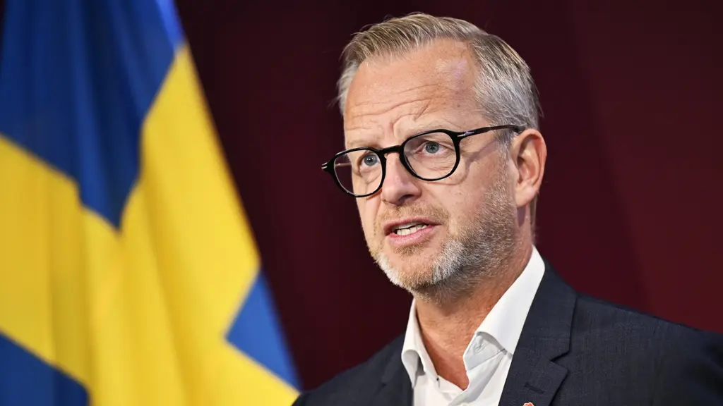 Mikael Damberg talar vid en pressträff i Stockholm om Socialdemokraternas ekonomiska politik. I bakgrunden syns Sveriges flagga mot röd fond.